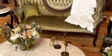 A vintage green tufted sofa and marble coffee table styled with floral arrangements and decorative items in a rustic setting.