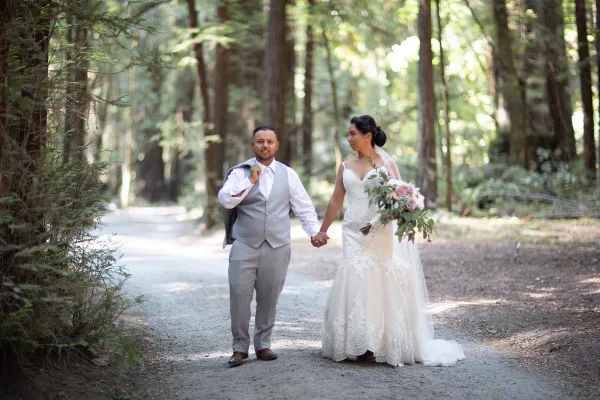 A bride and groom holding hands while walking down a forest path.