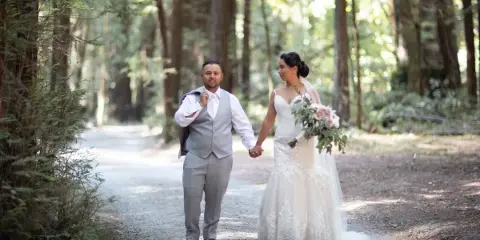 A bride and groom holding hands while walking down a forest path.