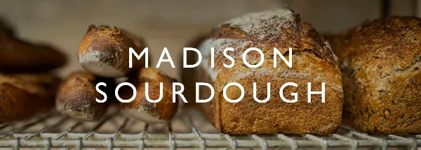 Artisan sourdough loaves resting on a wire cooling rack with the text 'MADISON SOURDOUGH' overlaid.