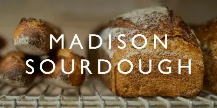 Artisan sourdough loaves resting on a wire cooling rack with the text 'MADISON SOURDOUGH' overlaid.