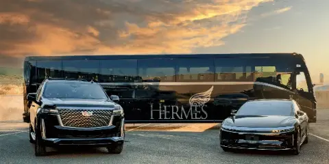 A black Hermes Worldwide coach, a black Cadillac SUV, and a black luxury sedan parked in a row at sunset.