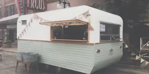 A vintage white camper trailer parked on a street, set up with a serving window and bunting.