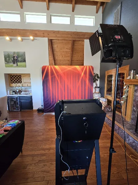 A professional mirror photo booth setup with a black booth unit, studio lighting, and a red curtain backdrop in an indoor venue.