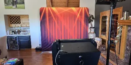 A professional mirror photo booth setup with a black booth unit, studio lighting, and a red curtain backdrop in an indoor venue.