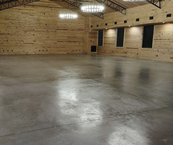 Interior view of a large event hall with knotty pine walls, polished concrete floors, and hanging chandeliers.