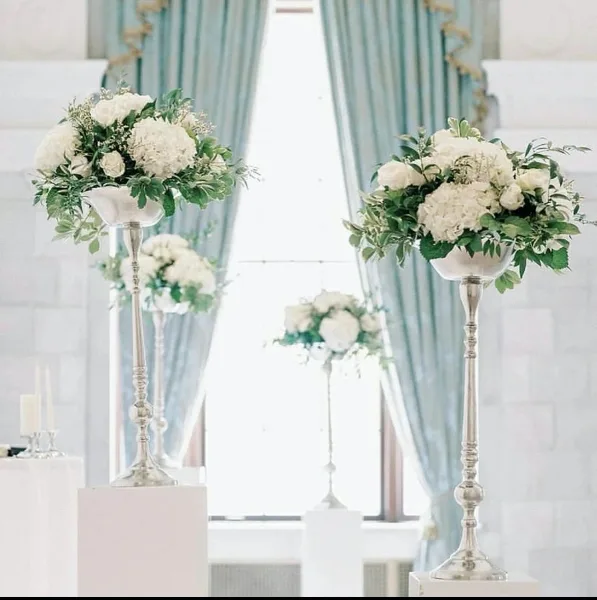 A wedding event setup featuring tall silver pedestals holding white floral arrangements and candles.
