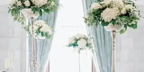 A wedding event setup featuring tall silver pedestals holding white floral arrangements and candles.