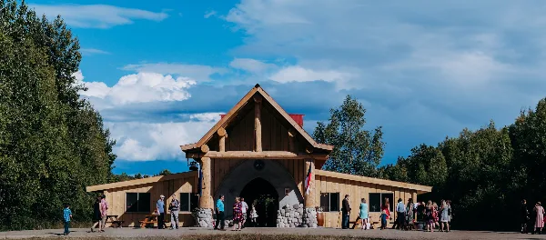 Exterior view of a rustic timber-frame barn venue with people gathered in front under a blue sky.