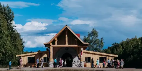 Exterior view of a rustic timber-frame barn venue with people gathered in front under a blue sky.