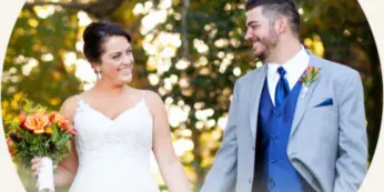 A bride in a white gown holding a bouquet and a groom in a light suit with a blue vest standing outdoors.