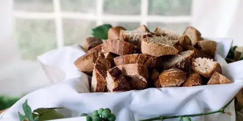 A white cloth-lined basket filled with rustic bread pieces, garnished with green grapes and leaves, accompanied by a small menu card.