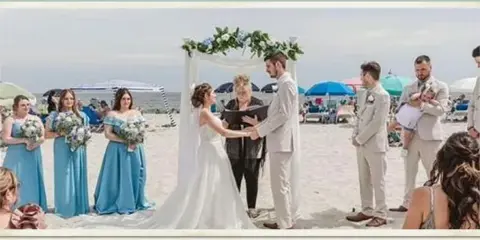 A wedding ceremony taking place on a beach with a bride, groom, officiant, and wedding party.