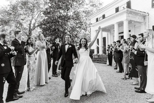 A black and white wedding photograph showing a bride and groom walking down an aisle while guests on either side blow bubbles.