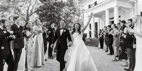 A black and white wedding photograph showing a bride and groom walking down an aisle while guests on either side blow bubbles.