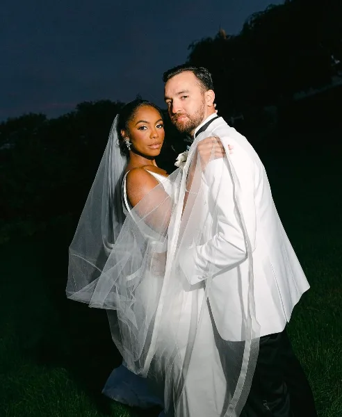 A bride and groom posing together, showcasing the groom's groomed beard and hair and the bride's makeup and hair styling.