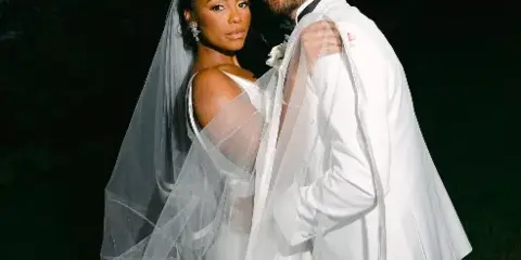 A bride and groom posing together, showcasing the groom's groomed beard and hair and the bride's makeup and hair styling.