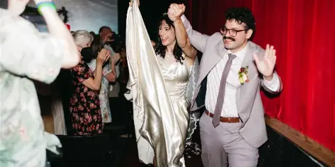 A bride and groom holding hands and walking down an aisle in a theater, captured in a candid, documentary style.