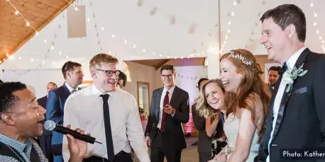 A bride and groom laughing and interacting with guests and a microphone at a wedding reception.