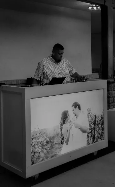 A DJ and MC standing behind a booth with a laptop and audio equipment.