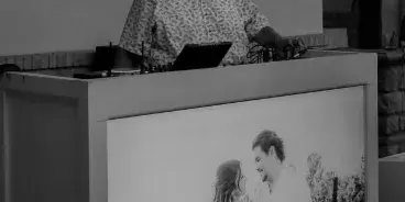 A DJ and MC standing behind a booth with a laptop and audio equipment.