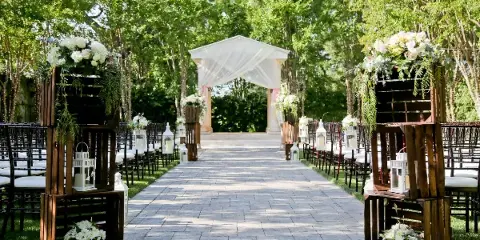 Outdoor garden wedding aisle with stone pavers, floral arrangements, and a white draped archway.