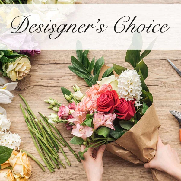 A hand holding a mixed flower bouquet with red roses, pink alstroemeria, and white blooms wrapped in brown paper.