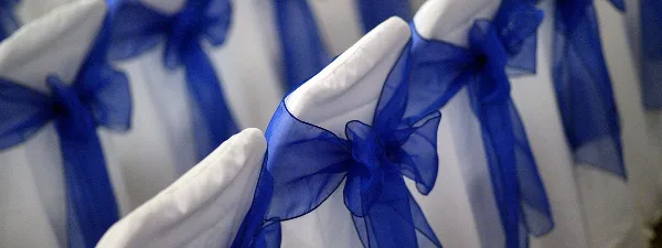 Close-up of white chair covers tied with blue sashes