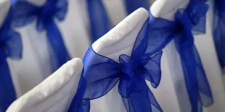 Close-up of white chair covers tied with blue sashes