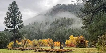 A wooden wedding ceremony arch and seating area on a grassy field with a misty mountain in the background.