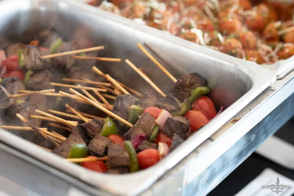 A close-up of a catering buffet featuring skewers of meat and vegetables in a stainless steel serving tray.