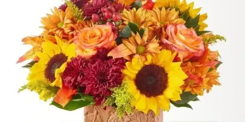 A floral arrangement with sunflowers, roses, and chrysanthemums in a textured vase.