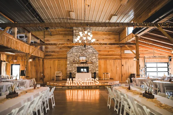 Rustic indoor wedding venue with wooden walls, stone fireplace, chandelier, and set banquet tables