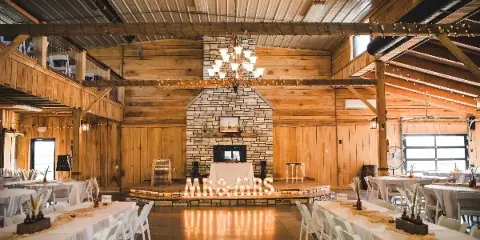 Rustic indoor wedding venue with wooden walls, stone fireplace, chandelier, and set banquet tables