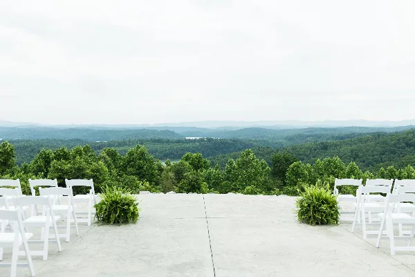 Outdoor wedding ceremony setup with white chairs overlooking a mountain and lake view.