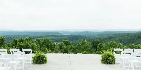 Outdoor wedding ceremony setup with white chairs overlooking a mountain and lake view.