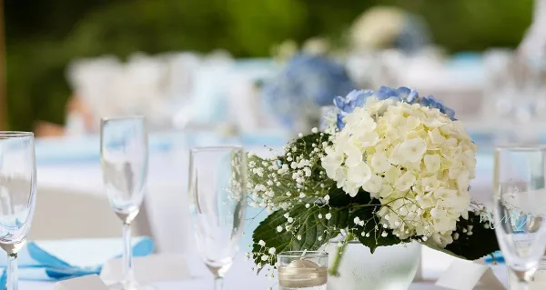 A close-up of a wedding table setting featuring white and blue hydrangeas, baby's breath, and champagne flutes.