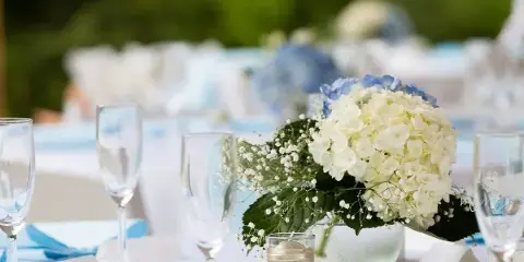 A close-up of a wedding table setting featuring white and blue hydrangeas, baby's breath, and champagne flutes.
