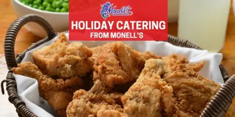 Basket of fried chicken with bowls of green peas and green beans and a glass of lemonade on a wooden table.