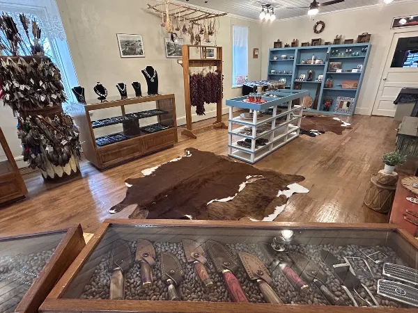 Interior view of a rustic general store with wooden floors, cowhide rugs, and displays of local crafts and jewelry.