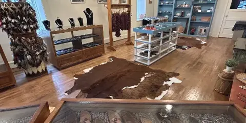 Interior view of a rustic general store with wooden floors, cowhide rugs, and displays of local crafts and jewelry.
