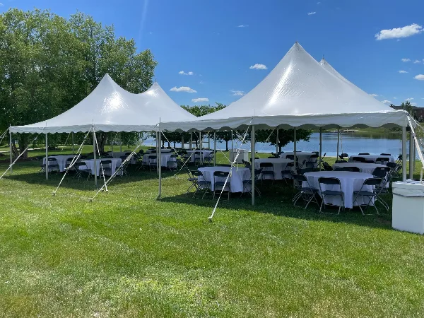 A large white event tent set up on a grassy lawn with round tables and chairs, near a body of water.