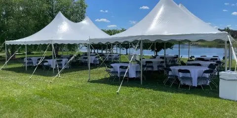 A large white event tent set up on a grassy lawn with round tables and chairs, near a body of water.