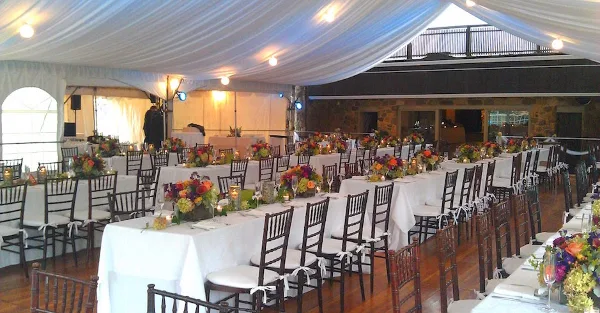 Interior of a large white event tent set up with rows of banquet tables, chairs, and floral centerpieces.