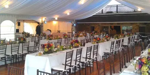 Interior of a large white event tent set up with rows of banquet tables, chairs, and floral centerpieces.