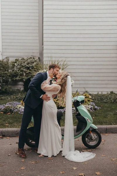 A bride and groom sharing a kiss next to a mint green scooter.