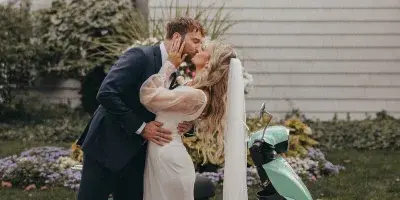 A bride and groom sharing a kiss next to a mint green scooter.