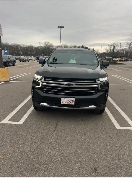 Front view of a black Chevrolet Suburban with a Massachusetts livery license plate parked in a parking lot.