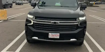 Front view of a black Chevrolet Suburban with a Massachusetts livery license plate parked in a parking lot.