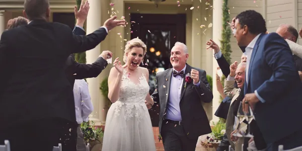 A bride and groom walking through a confetti shower with cheering guests at a wedding reception.